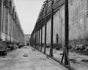 Historical WWII photograph inside the Camposanto Monumentale in Pisa, showing temporary wooden scaffolding and emergency protective roofing structures built to shelter medieval frescoes after the 1944 bombing.