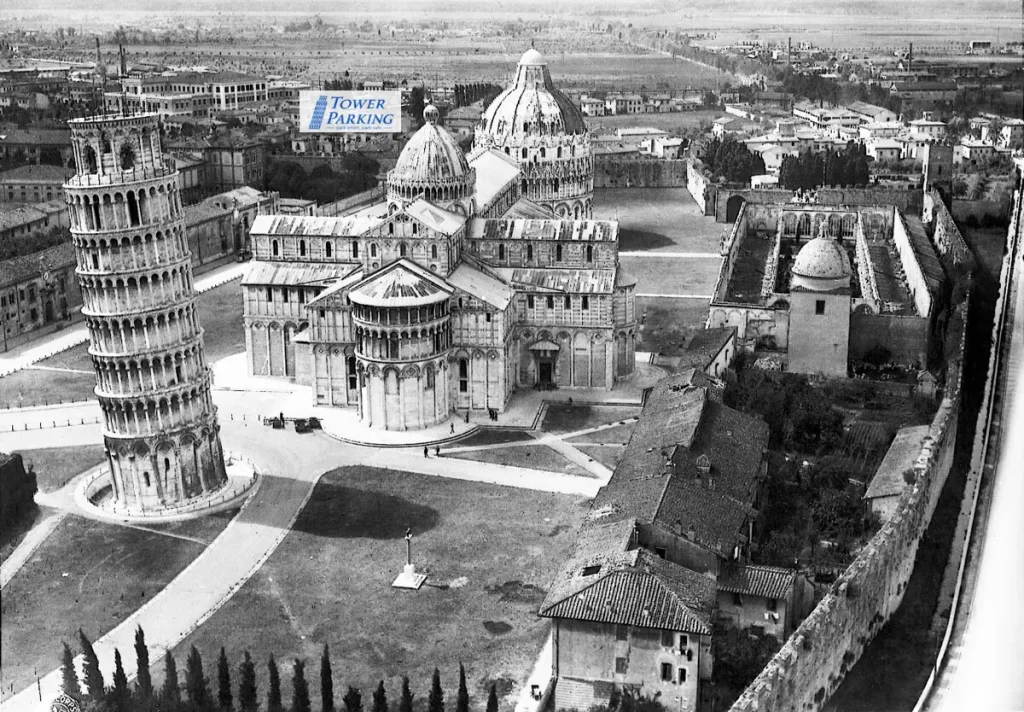Historical World War II aerial photo of the Piazza dei Miracoli in Pisa showing the destroyed, roofless Camposanto Monumentale after the 1944 bombing, with a graphic overlay marking the location of Tower Parking.