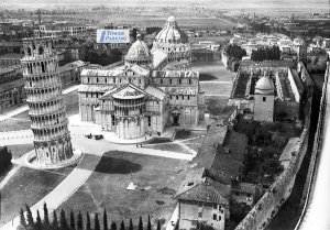 Historical World War II aerial photo of the Piazza dei Miracoli in Pisa showing the destroyed, roofless Camposanto Monumentale after the 1944 bombing, with a graphic overlay marking the location of Tower Parking.